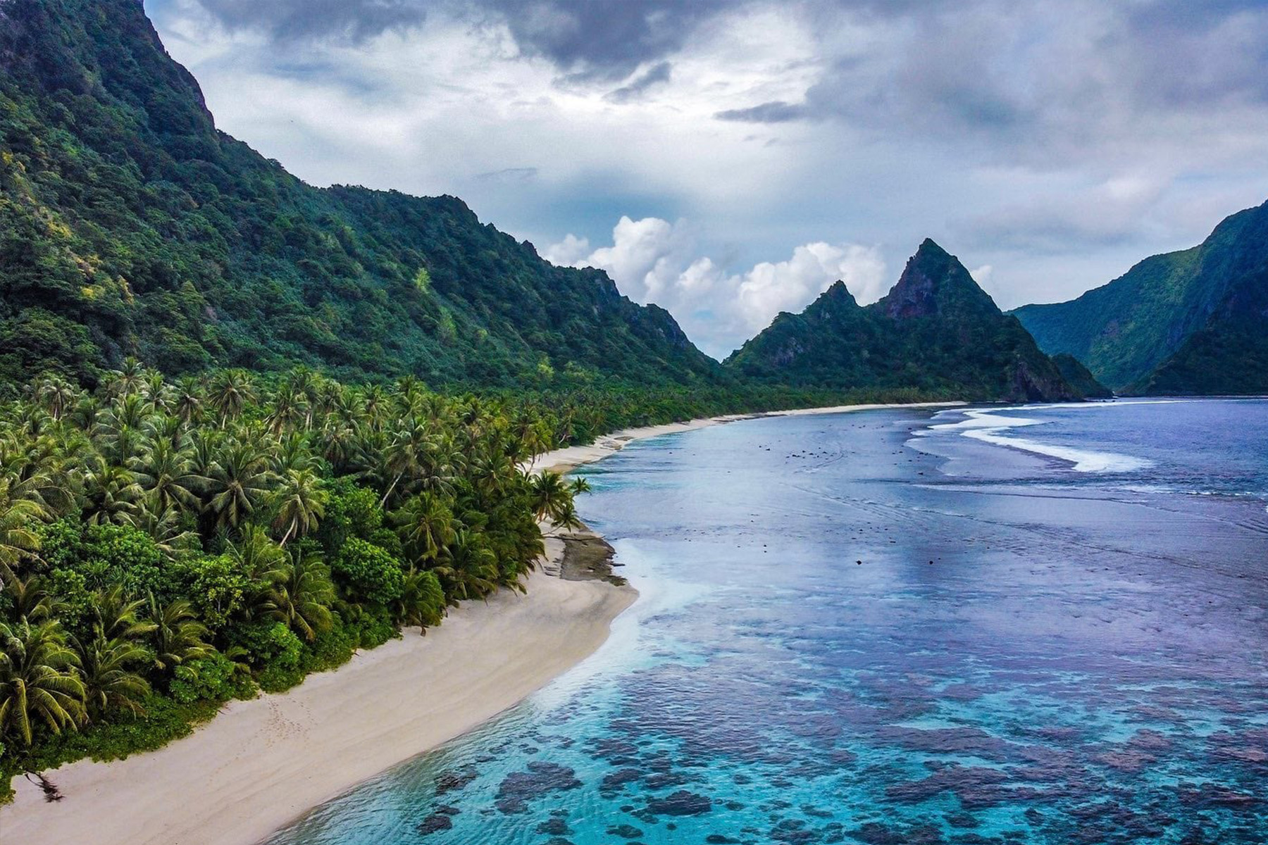 beach with corals surrounded by tall tropical mountains