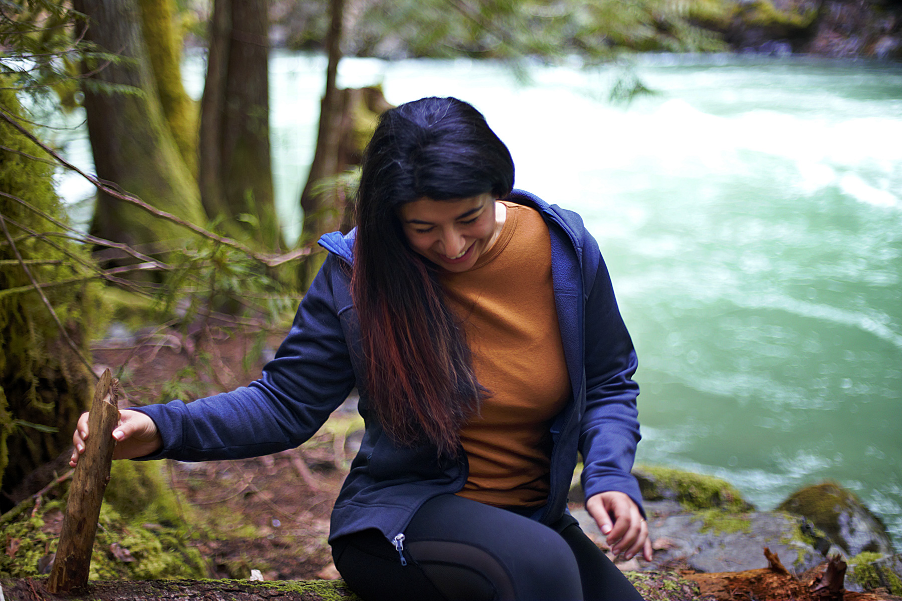 A woman sitting next to a stream in the forst.