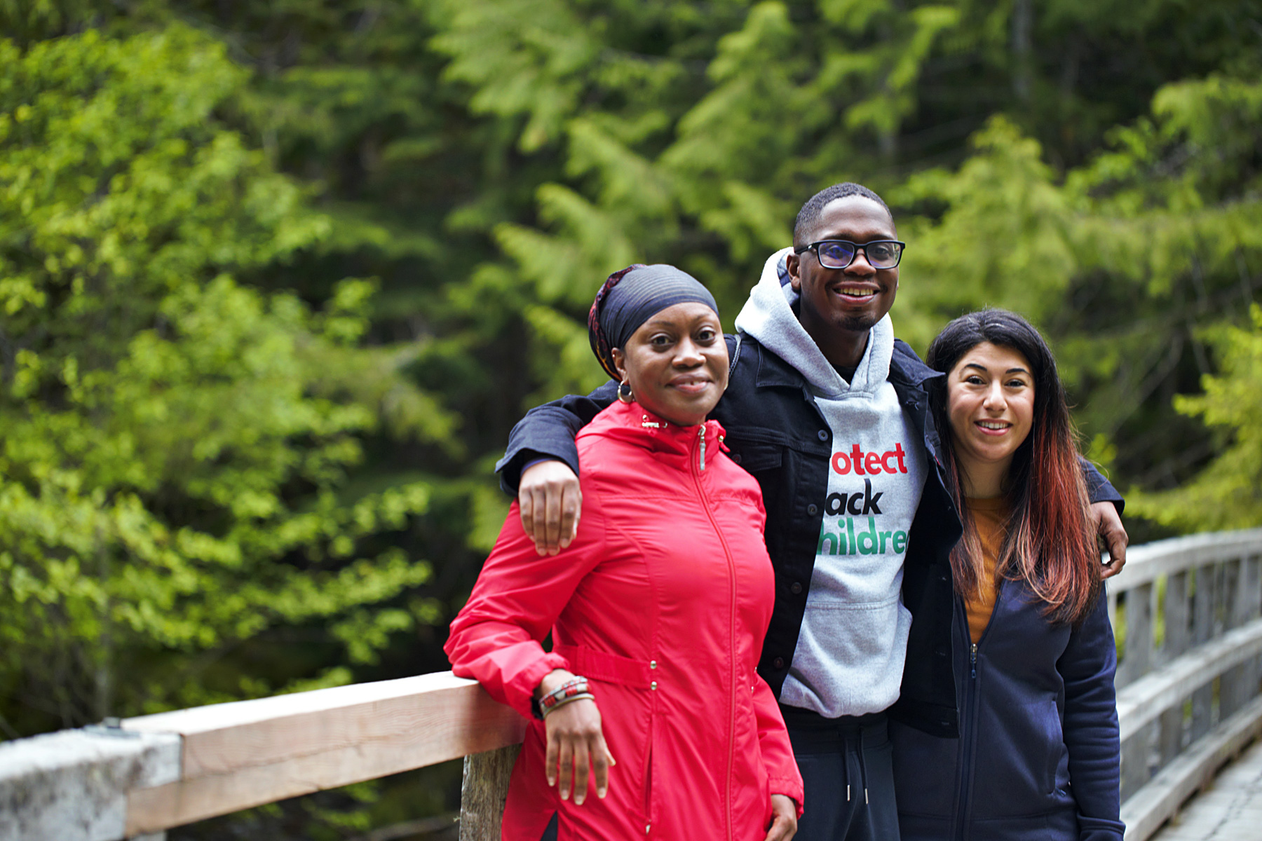 Three people on a bridge in a forest.