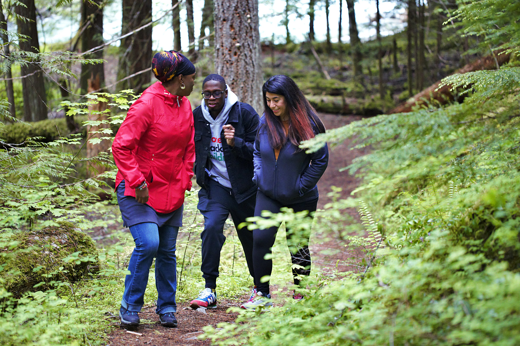 Three people walking on a trail through the woods.