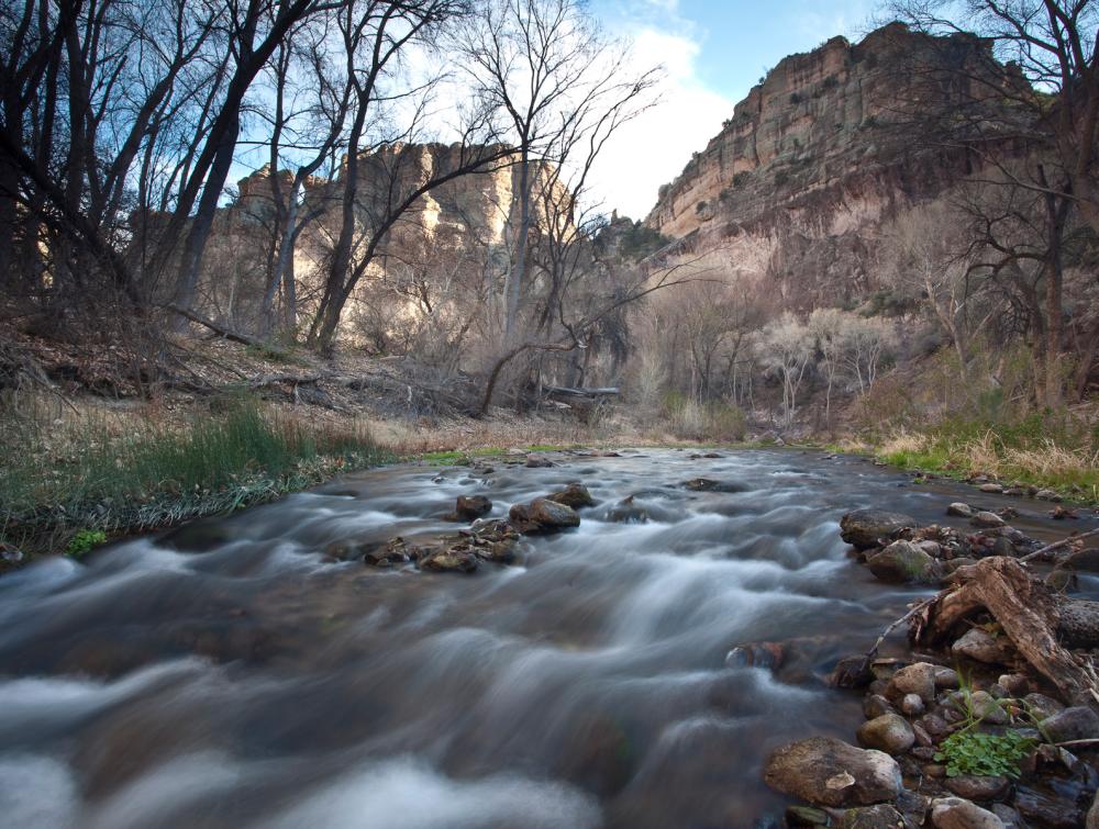 Creek fringed by trees rushes into the distance toward rocky buttes