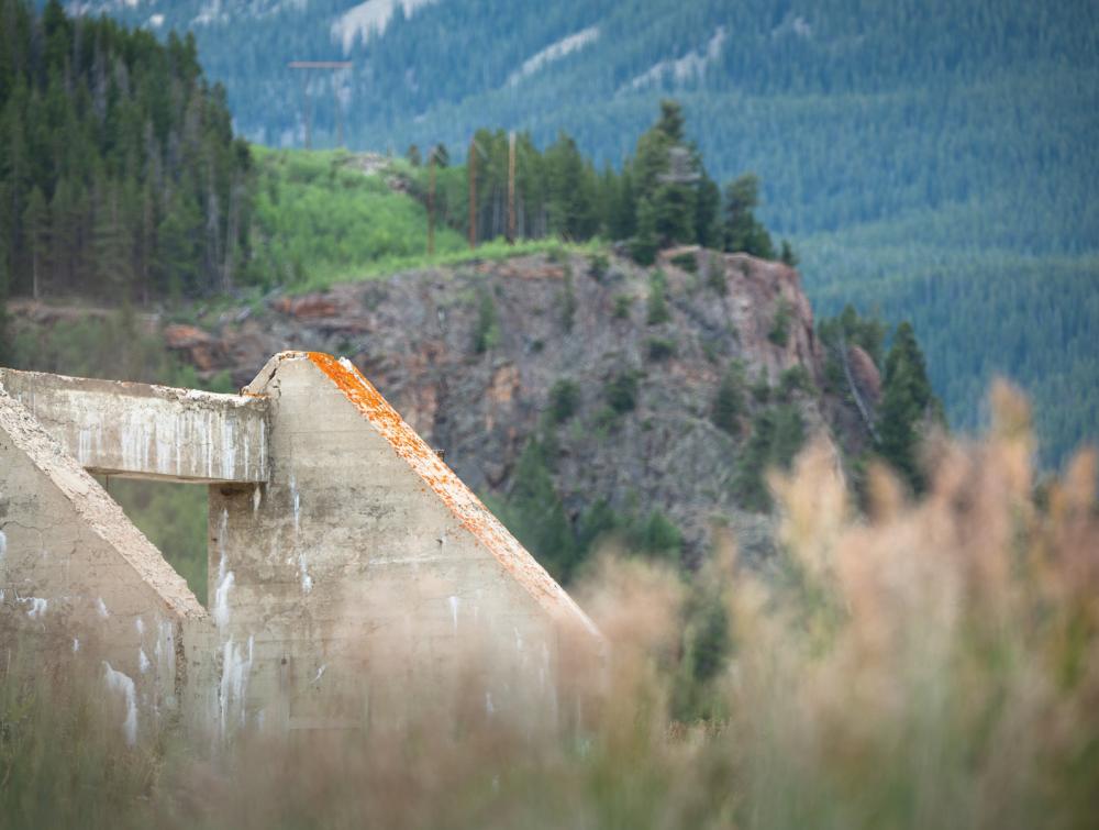 Concrete remains of building with grass in immediate foreground and alpine terrain in background at Camp Hale, Colorado
