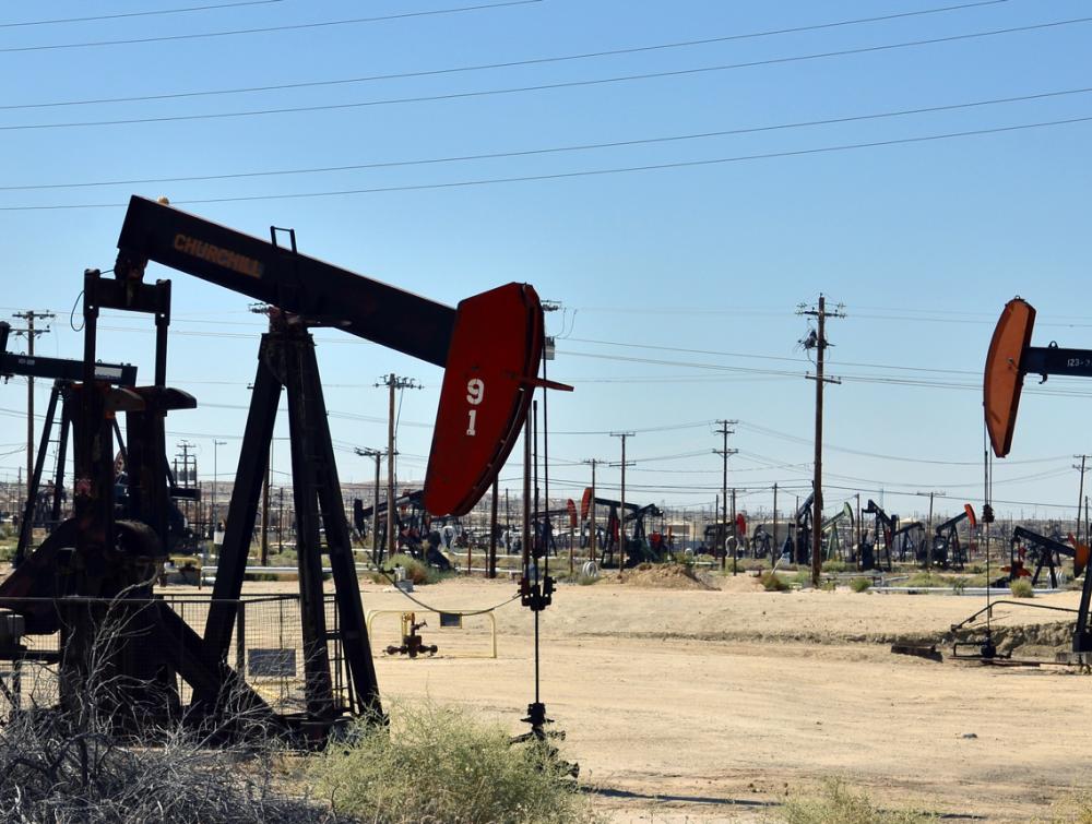 Oil pumps and transmission lines stretching to the horizon on flay, arid land in Bakersfield, California