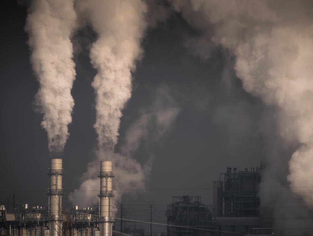 Smoke pouring out of two industrial smokestacks against a gray sky at Cherokee Generating Station