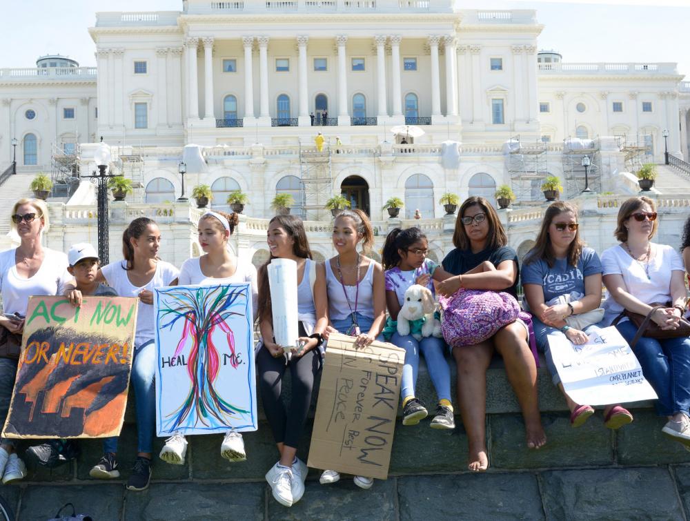 Women sitting on a short stone wall and holding placards in front of a white building