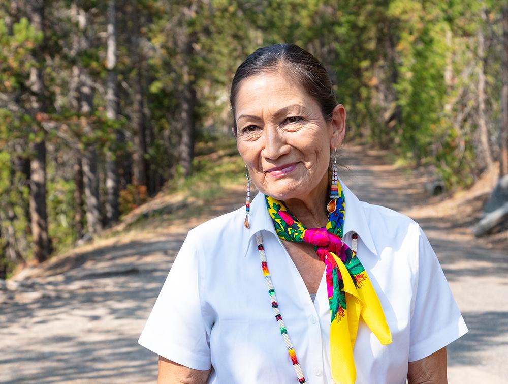 Interior Secretary Deb Haaland smiling in front of a forest.