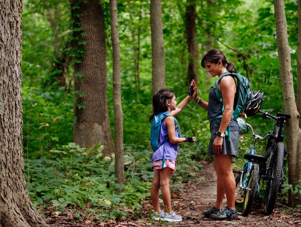 A woman and child high five during a break from bicycling along a forested trail