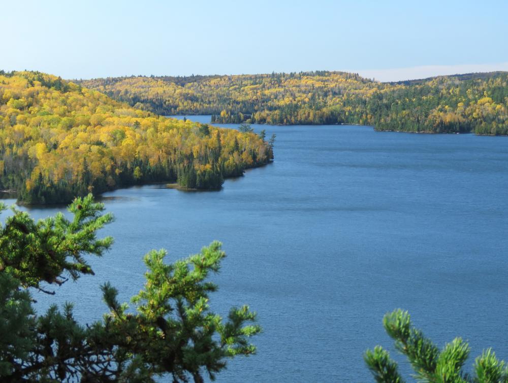 Clear blue lake surrounded by forest-covered hills where the trees are beginning to turn yellow and gold with autumn 