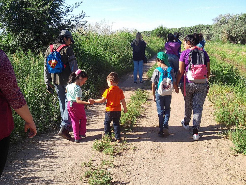 Two small children hold hands with other people while walking down a trail away from the camera