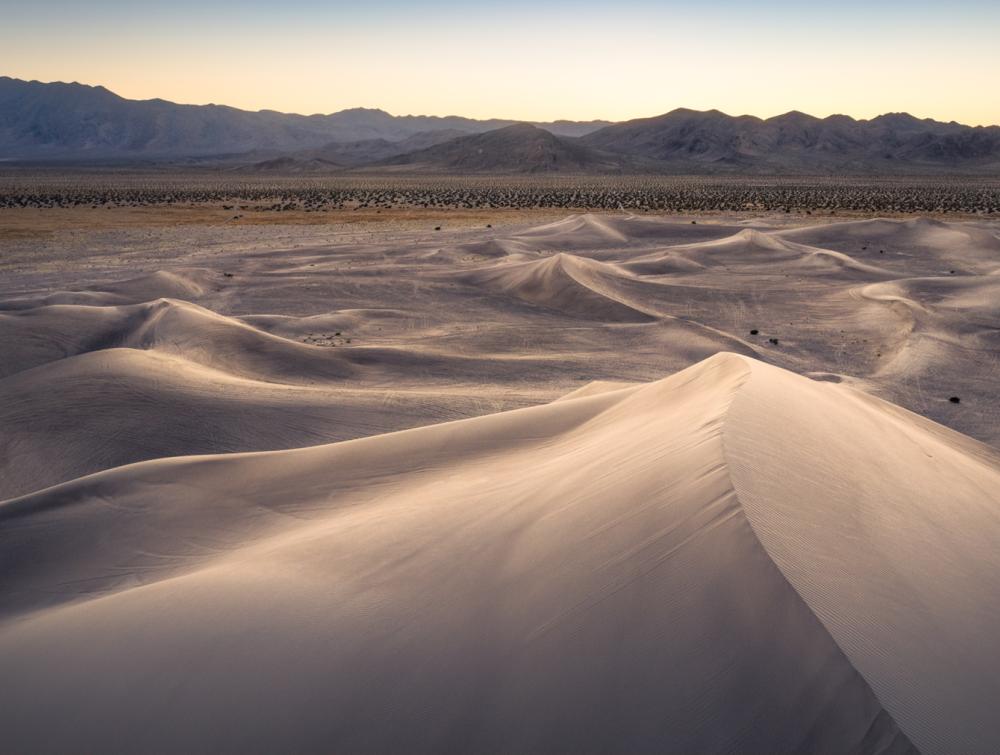 Pale-colored sand dunes with mountains visible on the horizon