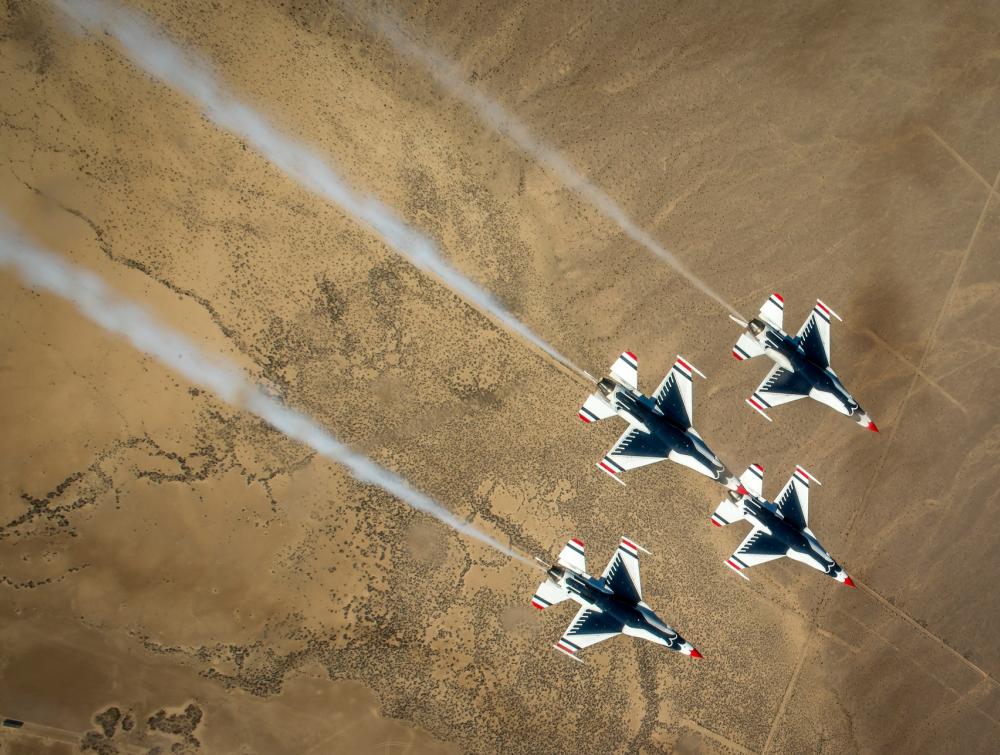 Overhead view of four military-style jets flying above a desert landscape