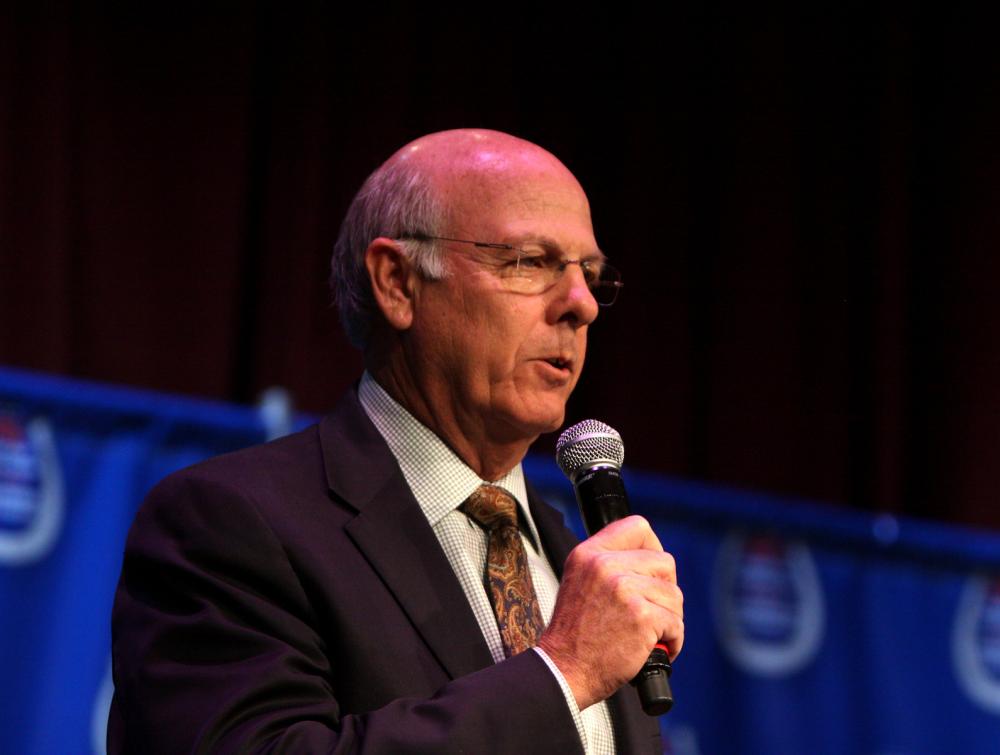 Man speaking into microphone standing in front of blue curtain