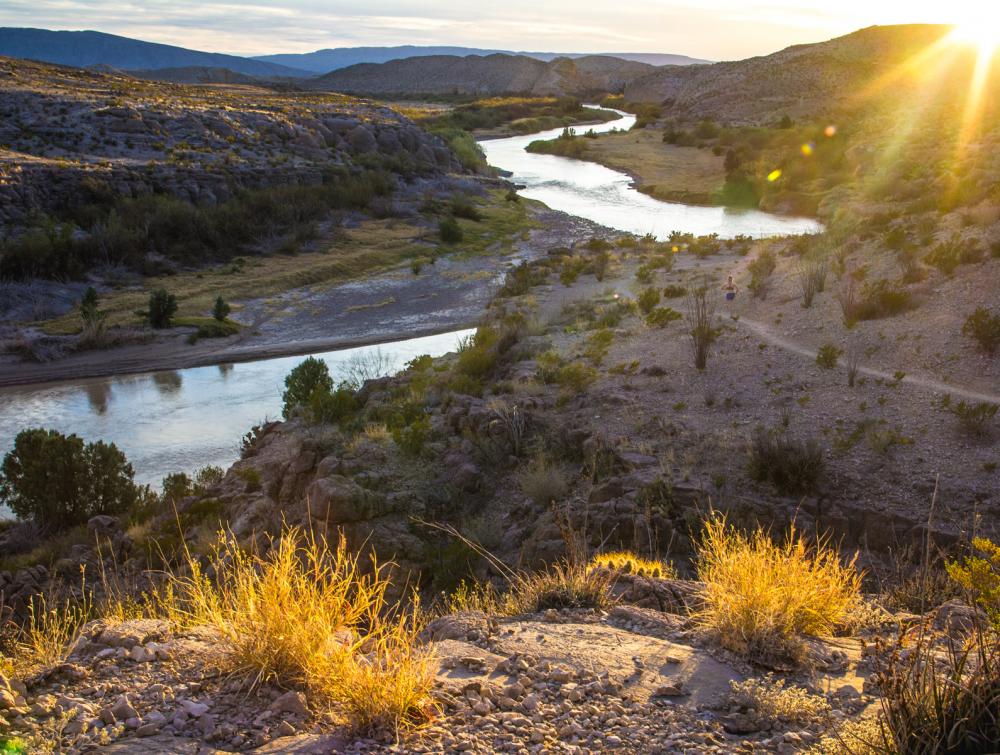 Sunset visible behind mountains and desert landscape with winding river