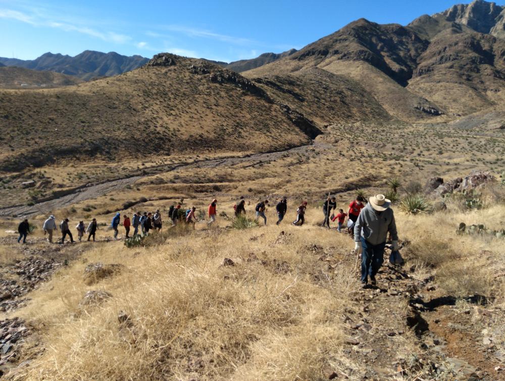 Procession of people hiking through mountainous desert landscape, with leader of the group near the foreground
