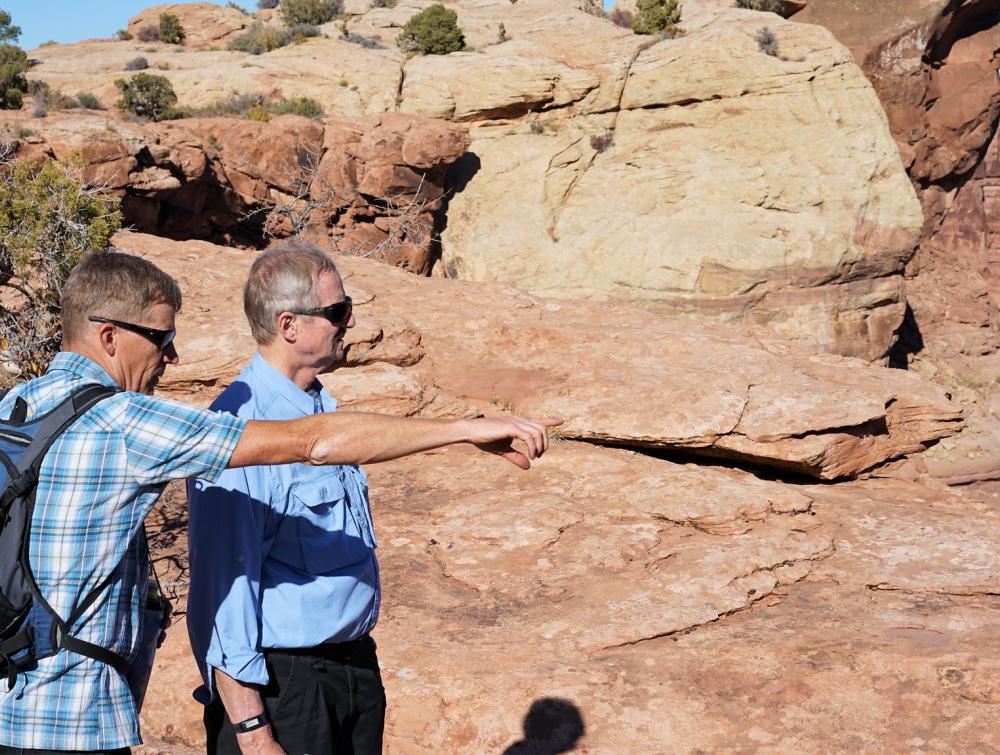 Two men look at something out of frame in front of a red-rock desert landscape in Moab, Utah