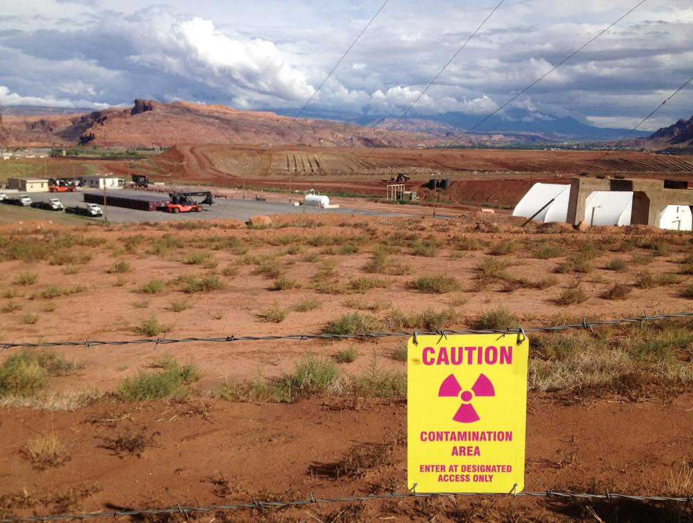 Sign reads "CAUTION - contamination area" in foreground of industrial site at the Moab Uranium Mill Tailings Remedial Action (UMTRA) project in Moab, Utah