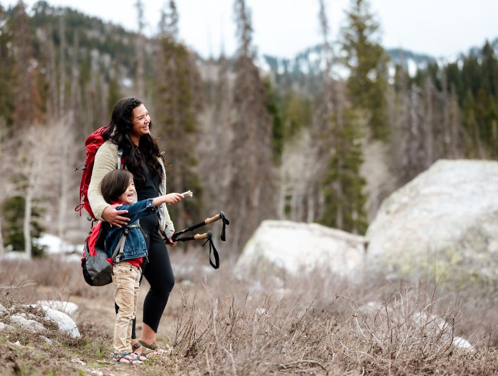 Backpacker stands with child in wooded area.
