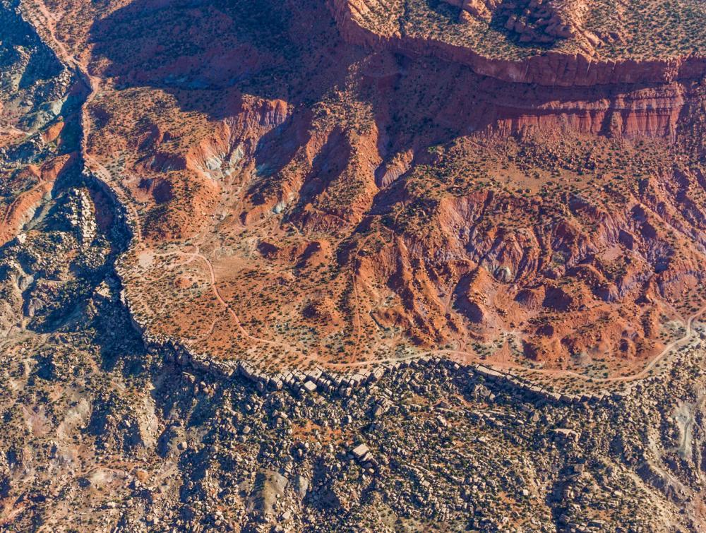 Aerial photo of craggy red-rock landscape including a mesa, dotted green trees 