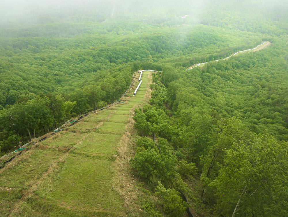 Aerial view of pipeline components lined up on verdant hillside near forests with fog in background