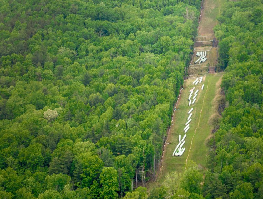Aerial view of pipeline components lined up on verdant hillside on path cut through forest 