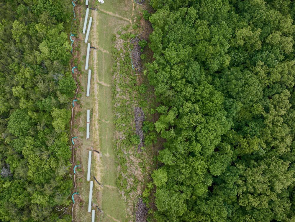 Aerial view of pipeline components lined up on verdant hillside on stripe of land cleared of forests growth