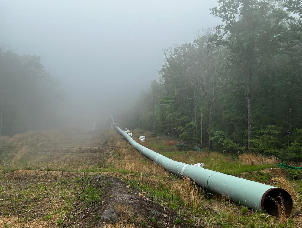 Under-construction pipeline receding into foggy distance with trees running alongside it