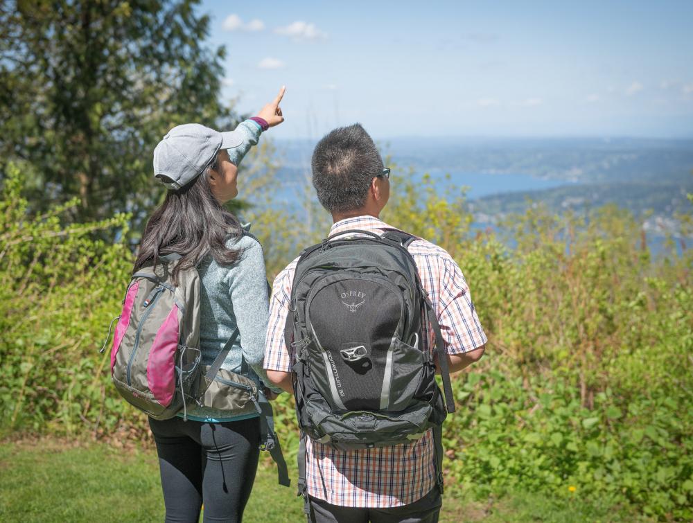 Two hikers with backpacks point to the sky surrounded by trees in King County, Washington