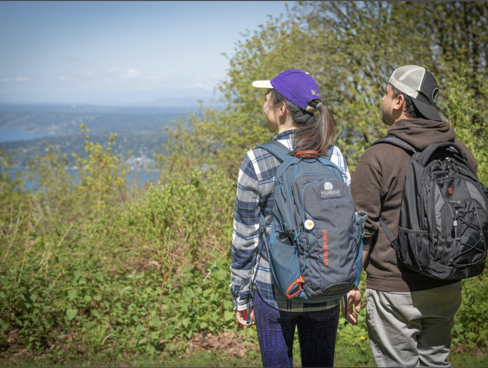 Two hikers in green park looking out at water view.