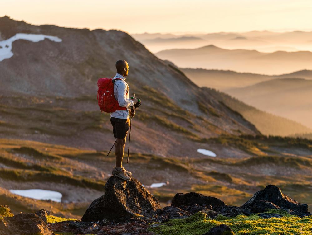 Lone hiker facing rays of sun in front of mountainous landscape in Mount Rainier National Park, Washington