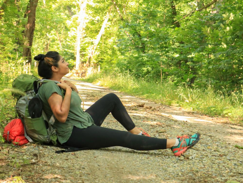 Person with backpack sitting on side of dirt trail in wooded area 