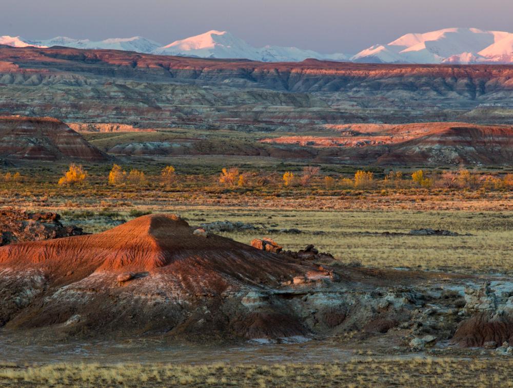 Multicolored buttes and plains landscape with snowcapped mountains in the background