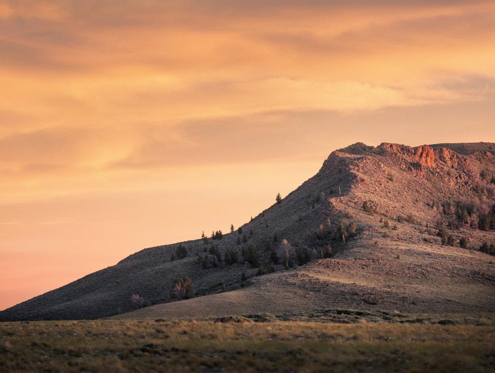 Butte rising above field with orange-tinted clouds in the background, Northern Red Desert, Wyoming