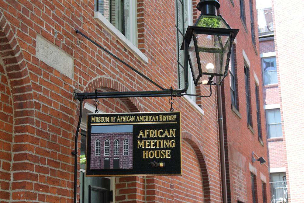 brick wall of building with a sign hanging from an external lamp that reads "museum of african american history: african meeting house"