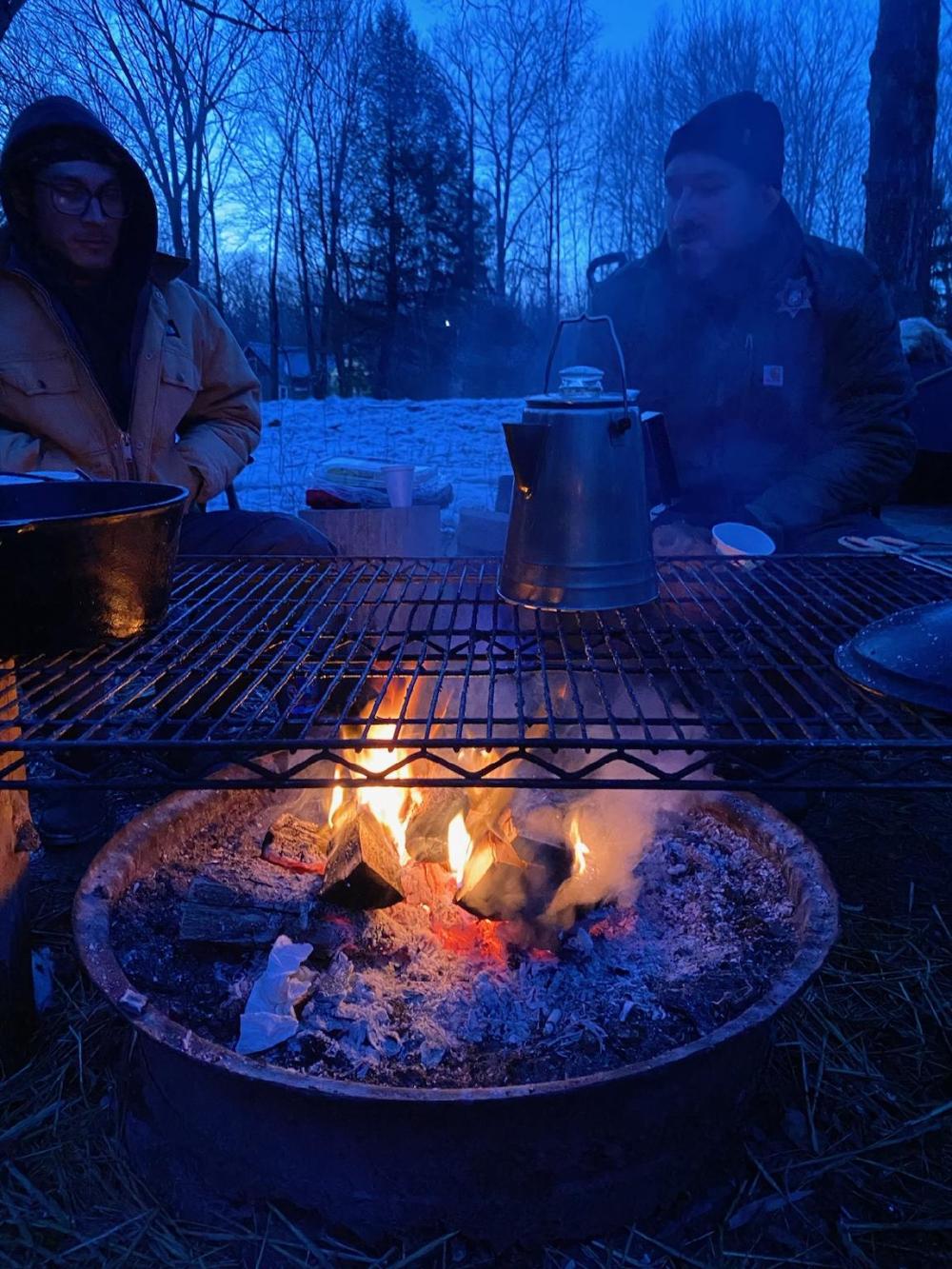 Two men, chat over a fire during a night with a deep blue tint.