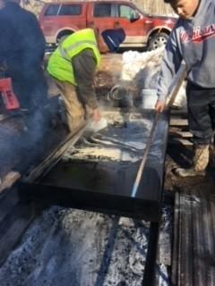 On a sunny day, a group works to transfer syrup (previously sap)