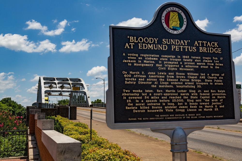 Historic marker with a title that reads "bloody sunday attack on edmund bridge", and a bridge with metal arches in the background