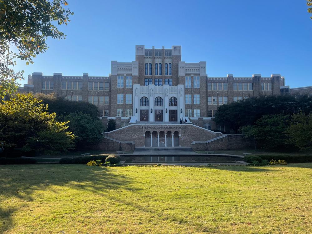 grass and a large brick structure with large windows and a small pond right in front 