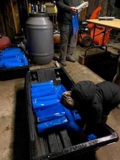 A person with a warm jacket on loads finished, brightly colored, sap collection bags in a sled