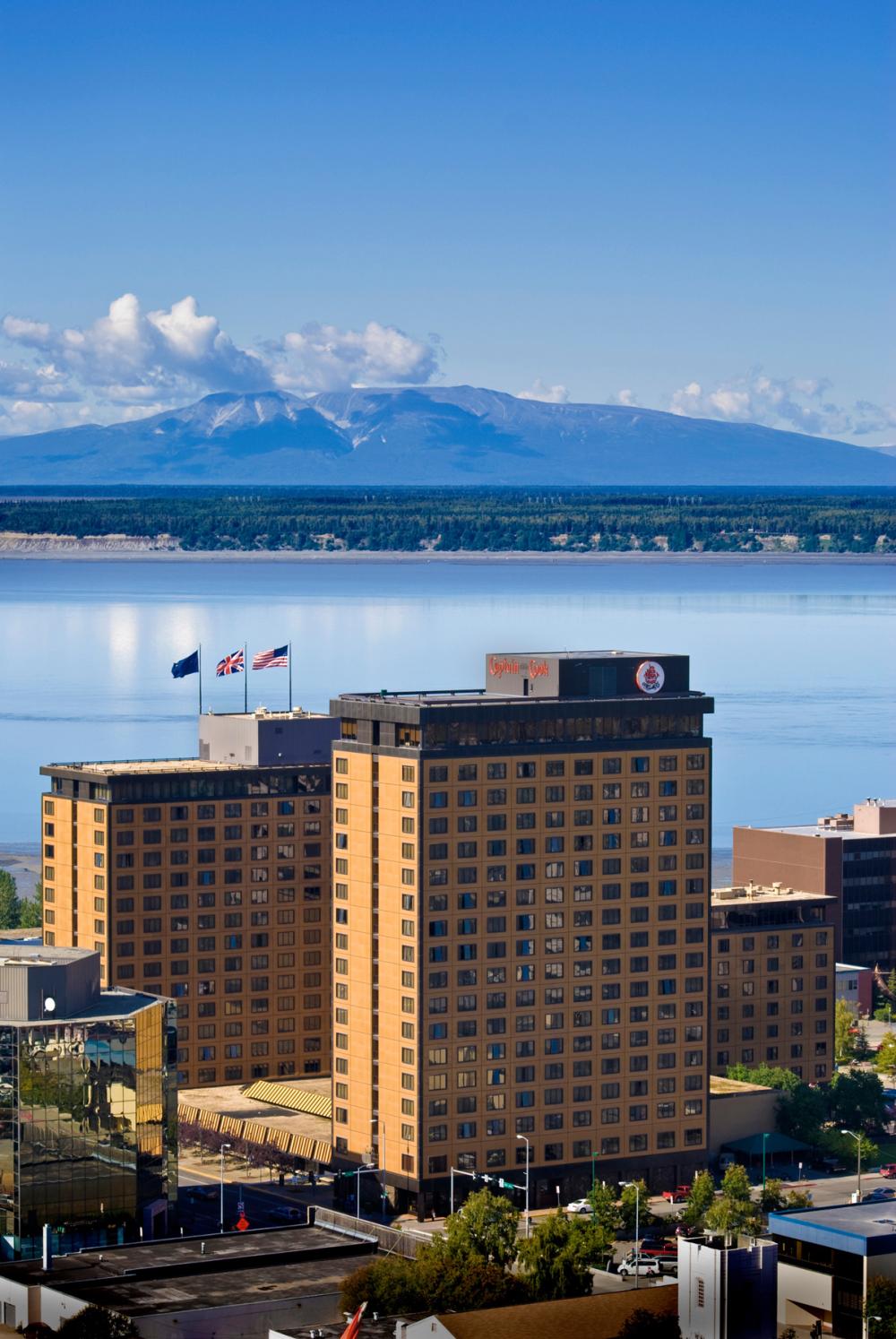 Brown hotel building in foreground with body of water and mountain visible behind it