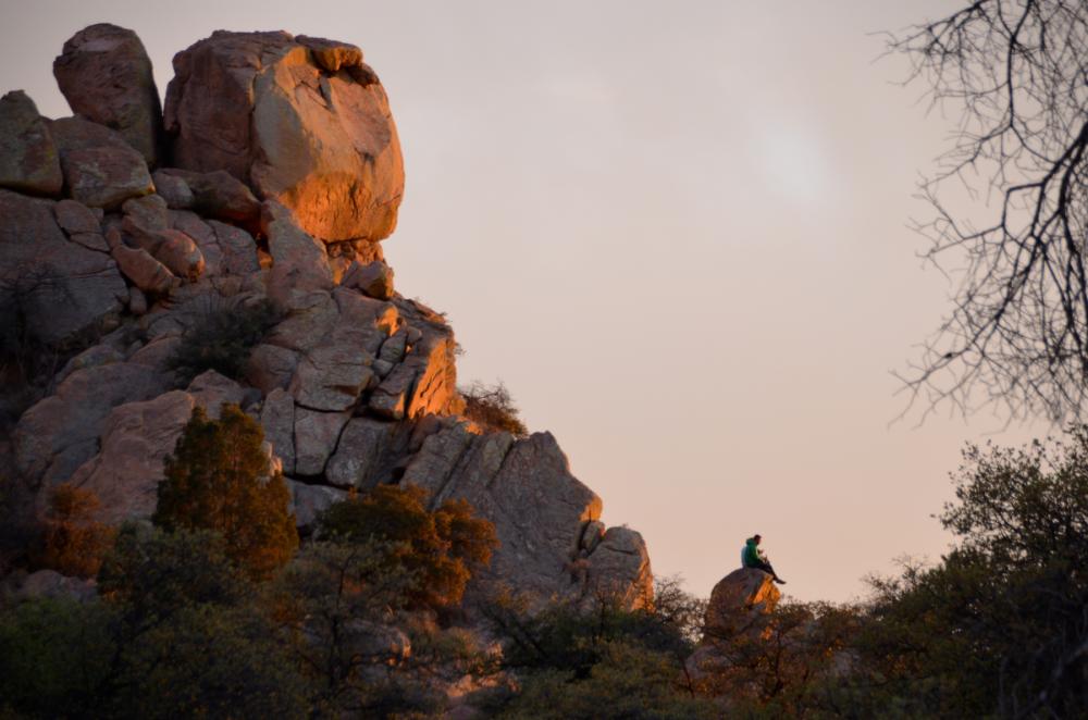 People sitting on boulder at base of large rocky formation at sunset, Coronado National Forest, Arizona