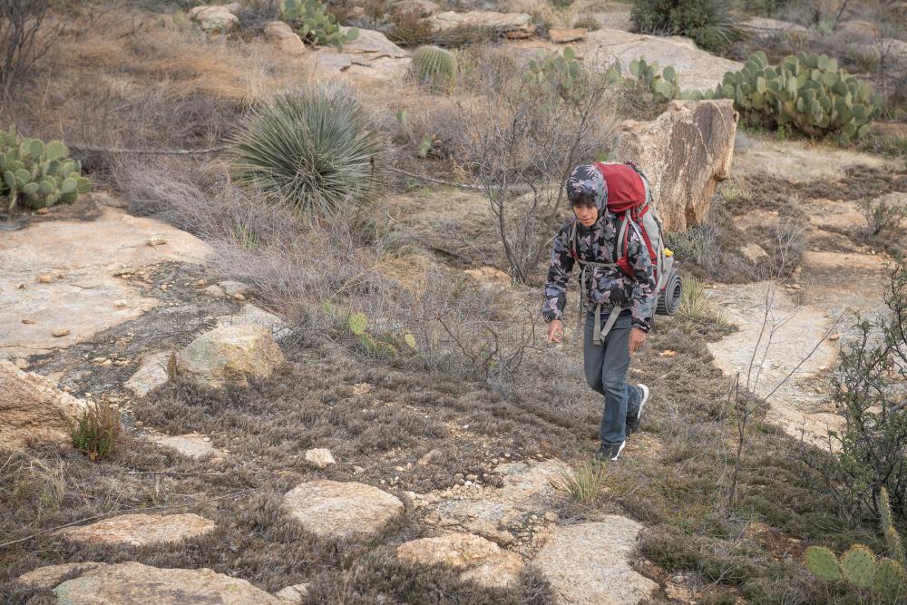 Young hiker walking over rocks and past desert plants in Saguaro National Park, Arizona