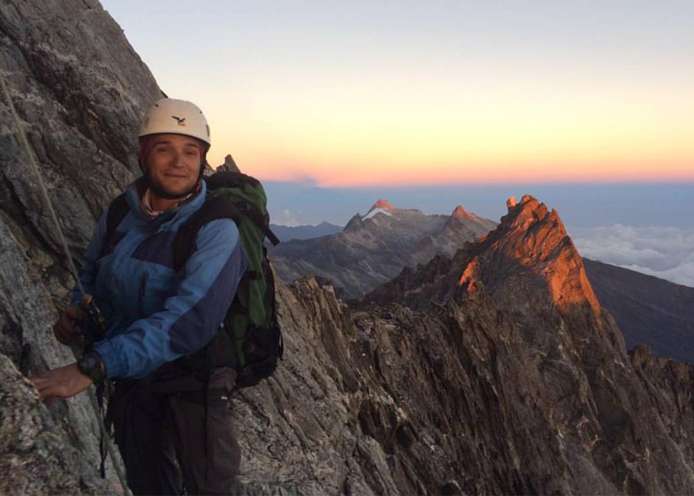 man with rock climbing gear, climbing a mountain, with sunrise in the background