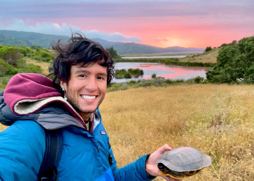 person taking selfie holding a turtle, on a vast prairie and the sun setting in the background