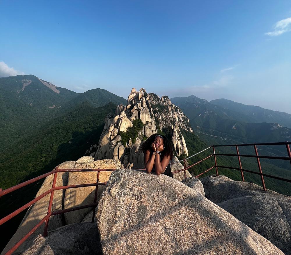 woman posing on a big rock, with mountains in the background