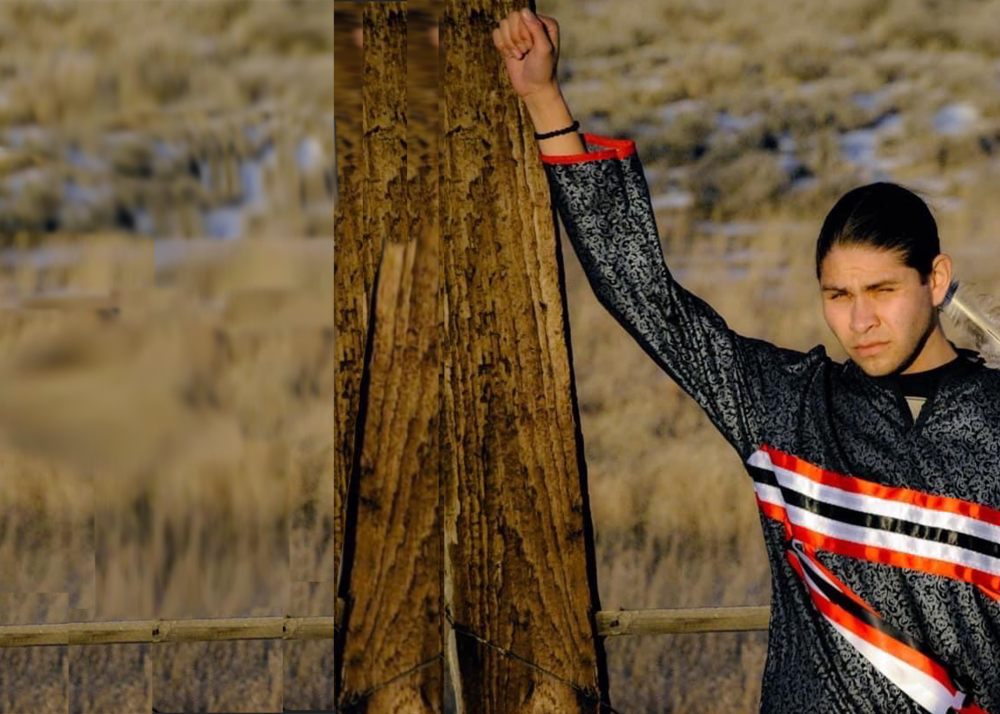 A two spirit person raises their fist in the air while standing outdoors 