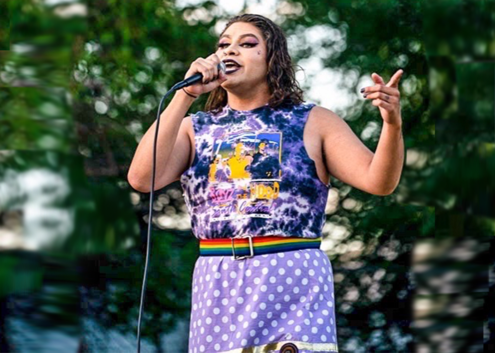 A two spirit person wears their hair down and speaks into a microphone