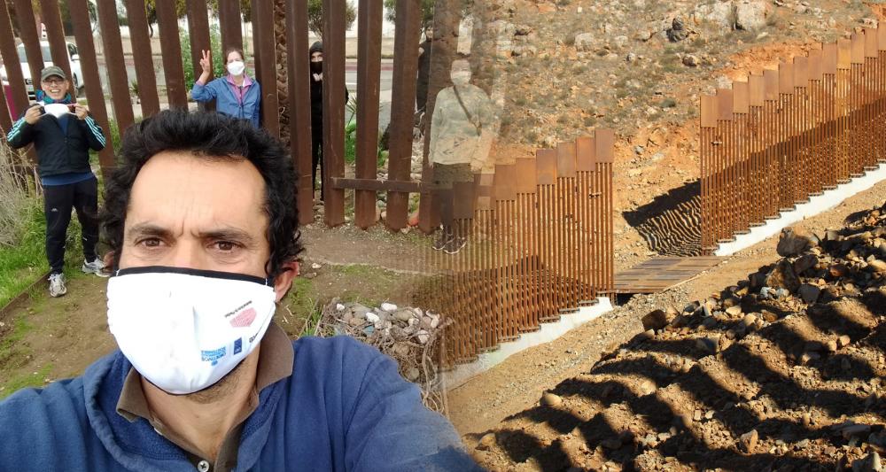 Left: Man wearing white surgical-style face mask. Right: Section of border wall under construction