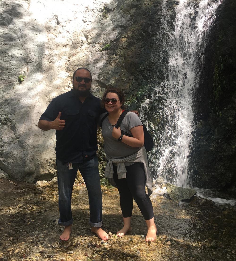 Two people standing and posing near a small waterfall