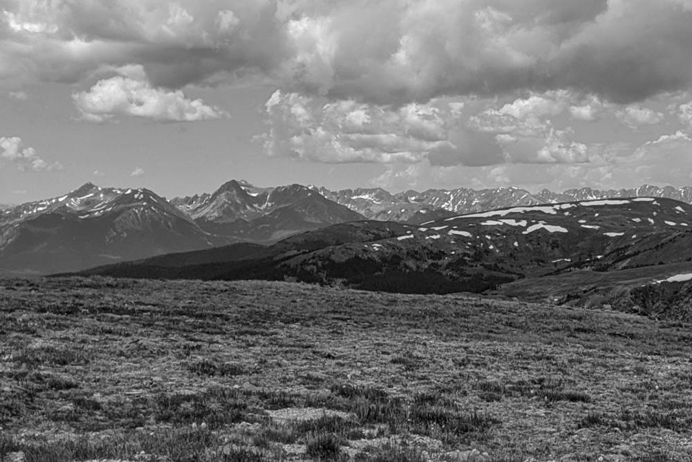 Black and white image of mountains with rocky meadow in foreground and clouds overhead