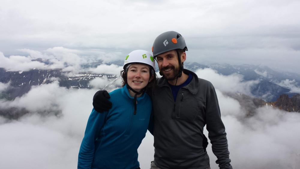 Two people posing with helmets on in front of cloudy backdrop